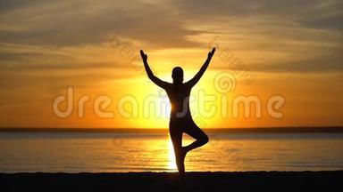 剪影女孩做树瑜伽姿势日落在自然户外。 运动瑜伽女子张开双臂练习
